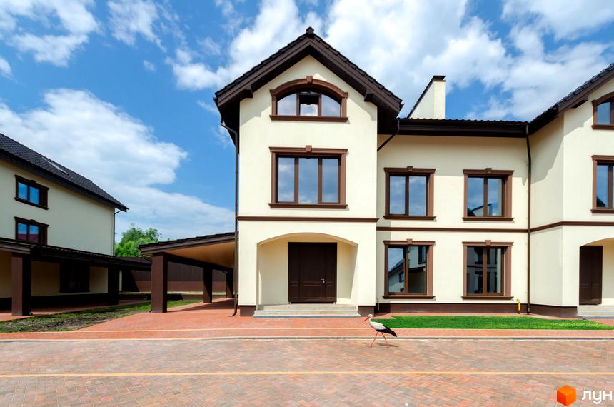 Котеджне містечко KM Vita Energy residence з білими фасадами та коричневими вікнами на тлі блакитного неба. Поруч розташований навіс для автомобілів та вимощена доріжка.