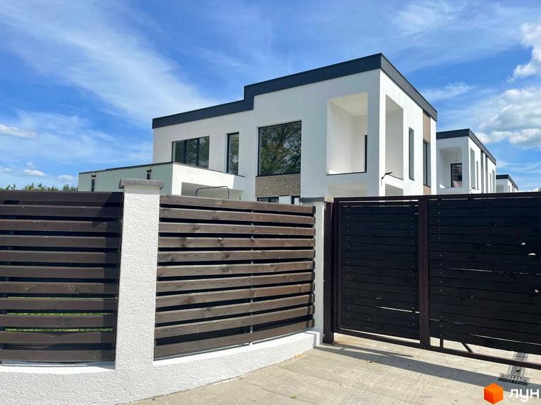 Котеджне містечко КМ Перлина Процева. Зовнішній вигляд білих будинків з темними дахами та дерев'яним парканом на прибудинковій території.