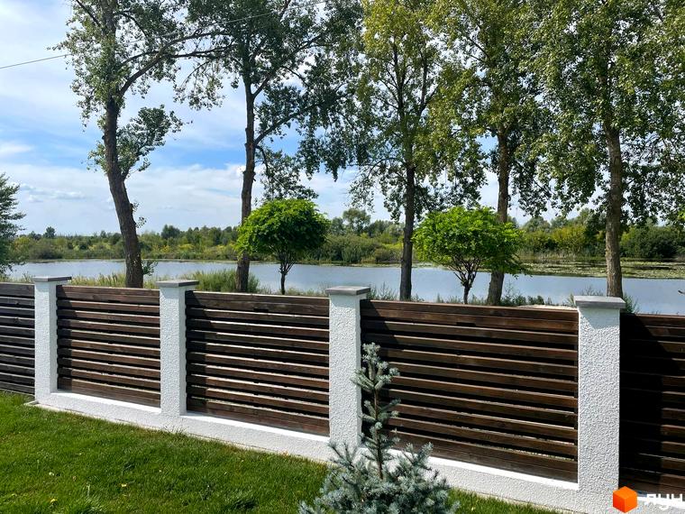 Котеджне містечко КМ Perlyna Protsiv з дерев'яним парканом та зеленою зоною біля водойми.