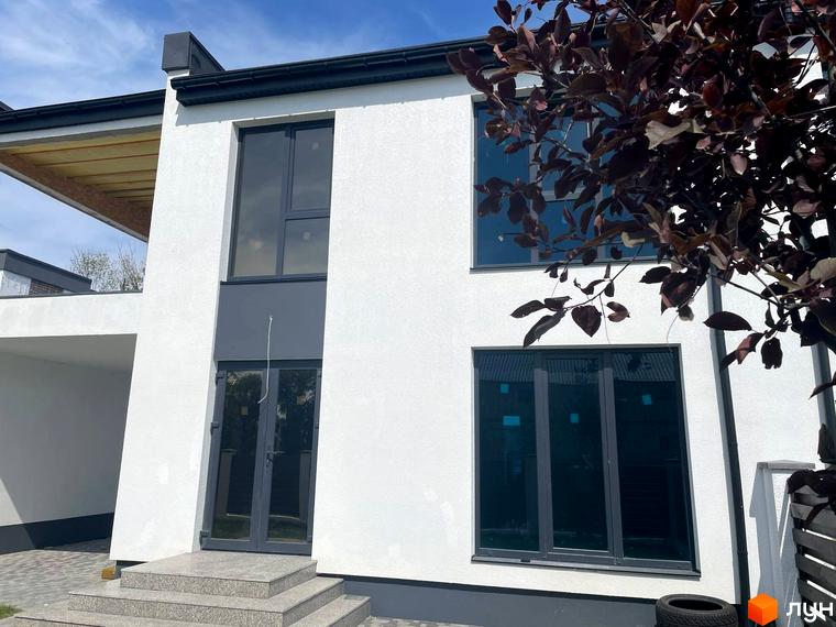 Котеджне містечко КМ Перлина Процева. Зовнішній вигляд двоповерхового будинку з великими вікнами та сірими дверима, прибудинкова територія з деревами.