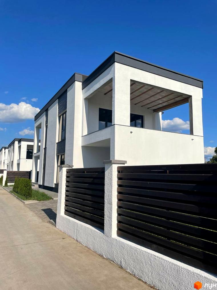 Котеджне містечко КМ Перлина Процева. Зовнішній вигляд будинків з білою штукатуркою, темними вікнами та навісами, огороджених темним парканом. Прибудинкова територія з бруківкою та зеленими насадженнями.