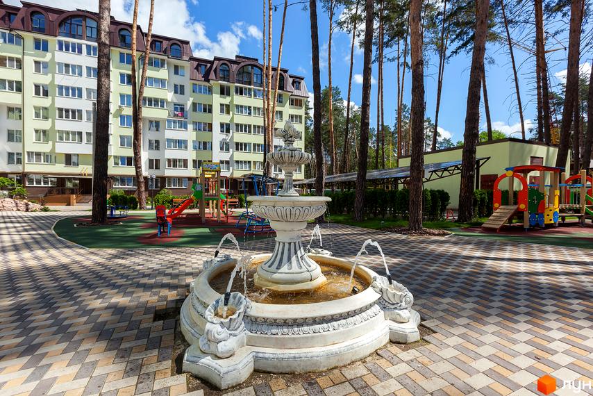 Житловий комплекс Ірпінські Липки. Багатоповерховий будинок світло-зеленого кольору з білими та сірими елементами. На прибудинковій території розташовані дитячий майданчик та фонтан.