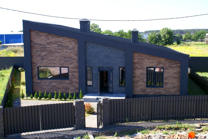 Зовнішній вигляд будинку КМ Country Villa з цегляним фасадом, темним дахом та парканом. На території розташовані зелені насадження та доглянутий двір.