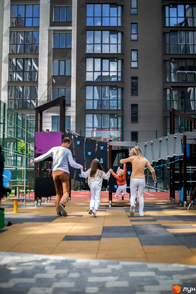 Житловий комплекс Паркова Алея з дітьми на ігровому майданчику. Вигляд новобудови з великими вікнами та облаштованою територією.