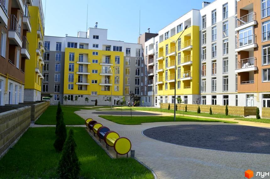 Зовнішній вигляд житлового комплексу ЖК Столичний з яскравими фасадами. Прибудинкова територія з зеленими насадженнями та зонами відпочинку.