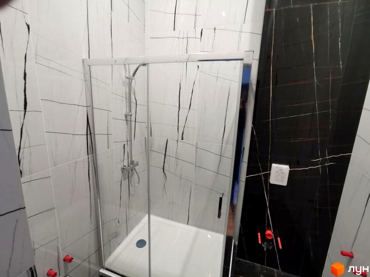 Сучасний душовий бокс у ванній кімнаті з білою плиткою та чорними прожилками, що доповнює дизайн чорної мармурової стіни.