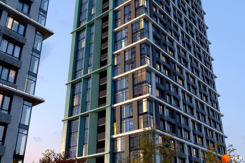 Зовнішній вигляд новобудови ЖК Central Hills з панорамними вікнами та балконами на тлі ясного неба. Будівельний проєкт має багатоповерхові будівлі з фасадами сірого та бірюзового кольору.