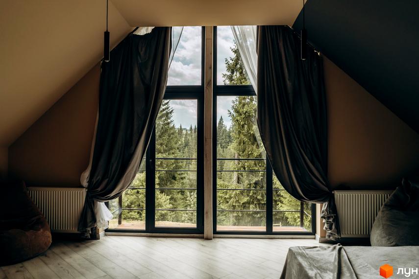 Вікно з шторами в кімнаті з видом на ліс. КМ Gutenberg – це житловий комплекс з мальовничими краєвидами.