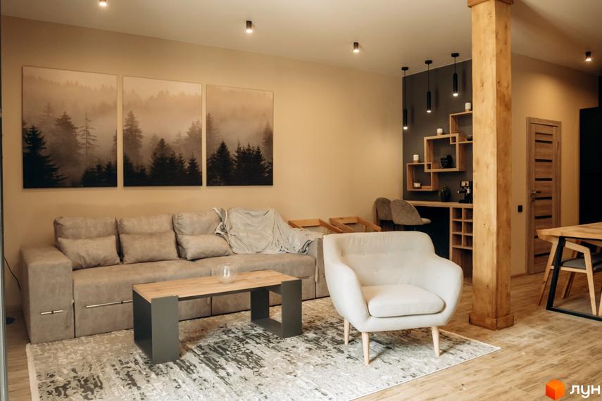 Інтер'єр вітальні в житловому комплексі КМ Gutenberg з диваном, кріслом та картинами з лісом. Затишна атмосфера для відпочинку та сімейного дозвілля.
