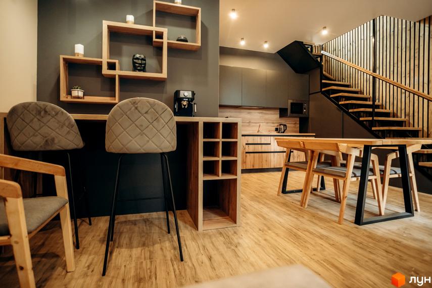Інтер'єр кухні-вітальні в житловому комплексі КМ Gutenberg з барною стійкою, стільцями та обіднім столом. Дизайн виконаний в сучасних тонах з дерев'яними елементами.