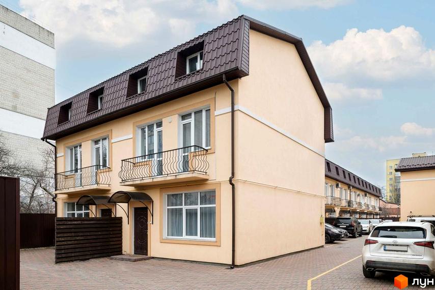 Таунхауси „Родинний Преміум 2“ – двоповерхові будинки з коричневим дахом та балконами, розташовані на бруківці біля паркану.