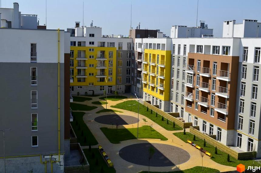 Житловий комплекс Столичний з яскравими жовтими та сірими фасадами. На прибудинковій території зелені газони та доріжки.