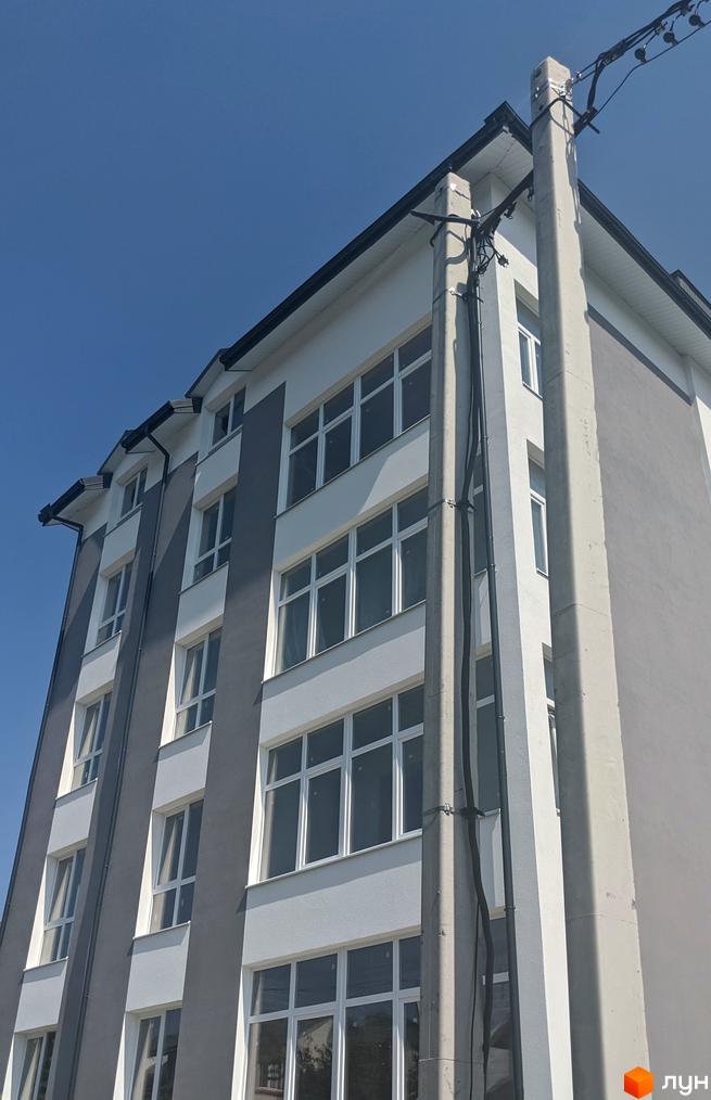 Зовнішній вигляд новобудови на вул. Крип'якевича з сірими та білими фасадами та великими вікнами. Будинок має кілька поверхів.