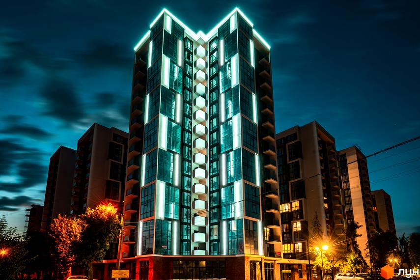 Житловий район Manhattan: сучасна архітектура з підсвічуванням вночі, вікна та балкони, що виходять на вулицю. Навколо зелені дерева та вуличне освітлення.