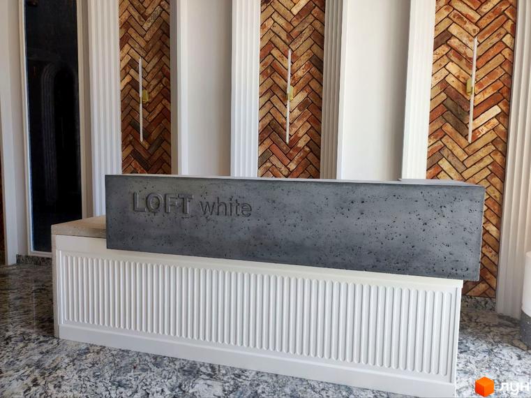 Рецепція новобудови Loft White з бетонною стійкою та написом. Інтер'єр приміщення має цегляну стіну та декоративні колони.