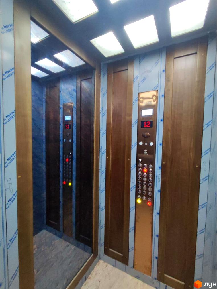 Інтер'єр ліфта в житловому комплексі Loft White з дерев'яними панелями та кнопковою панеллю з цифровим дисплеєм.