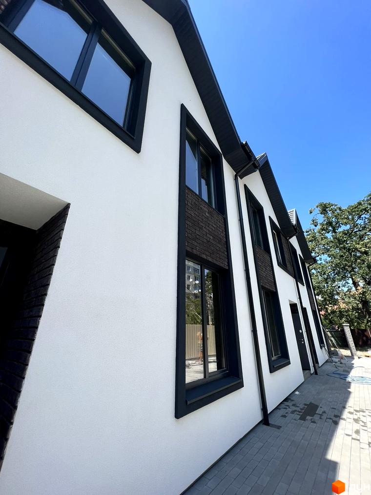 Фасад Таунхаусів М1 з білою штукатуркою, темними вікнами та цегляними вставками. Перед будинком укладена бруківка.