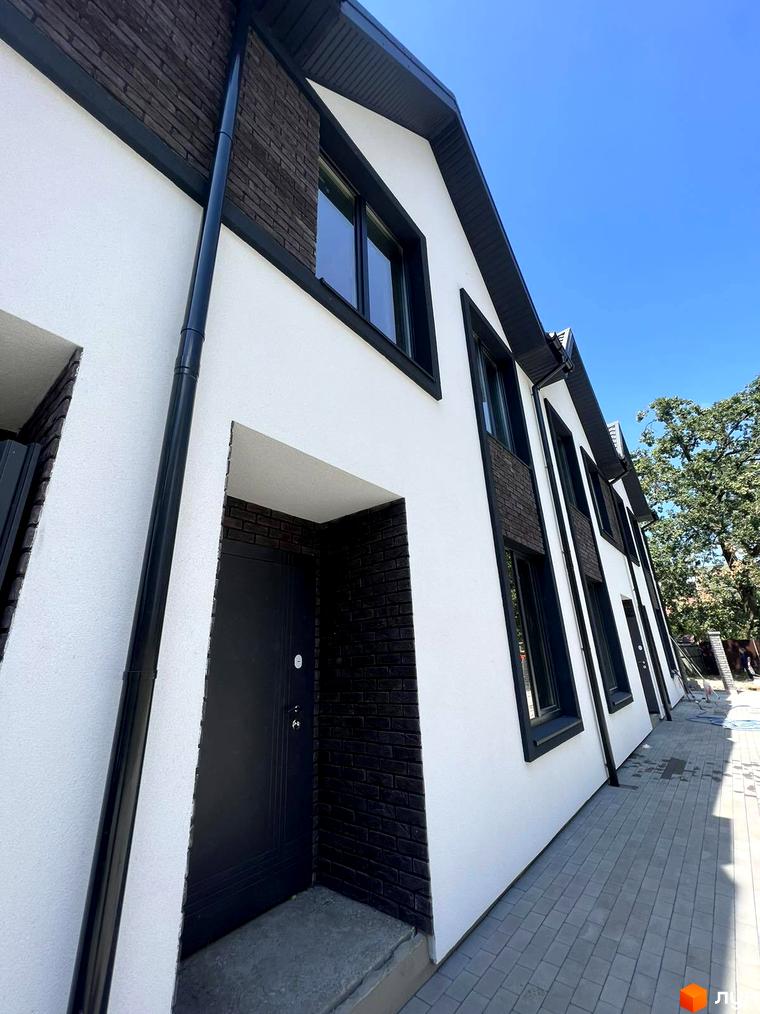 Білий фасад Таунхаусів М1 з темними віконними рамами та цегляними вставками. Перед будинками викладена сіра тротуарна плитка.