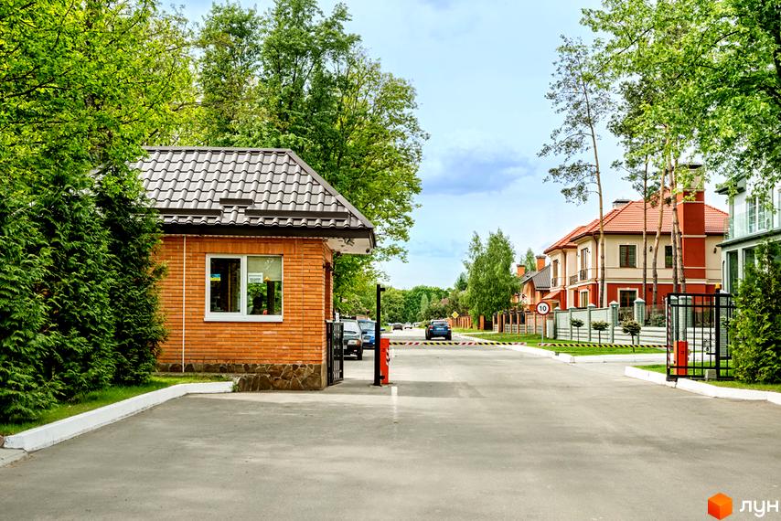 В'їзд до житлового комплексу КМ Парк хаус з охороною, поруч зелені насадження та сучасні будинки.