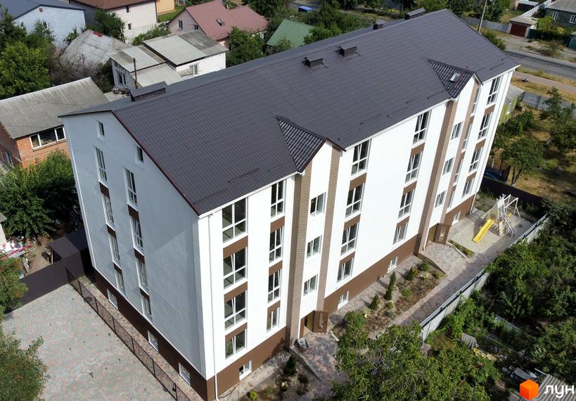 Будинок житлового комплексу SMART IDEA з біло-коричневим фасадом та темним дахом. Поруч дитячий майданчик та зелені насадження.