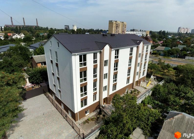 Новобудова ЖК SMART IDEA з біло-коричневим фасадом та темним дахом. Поруч розташований двір з дитячим майданчиком та вимощеною плиткою територією.