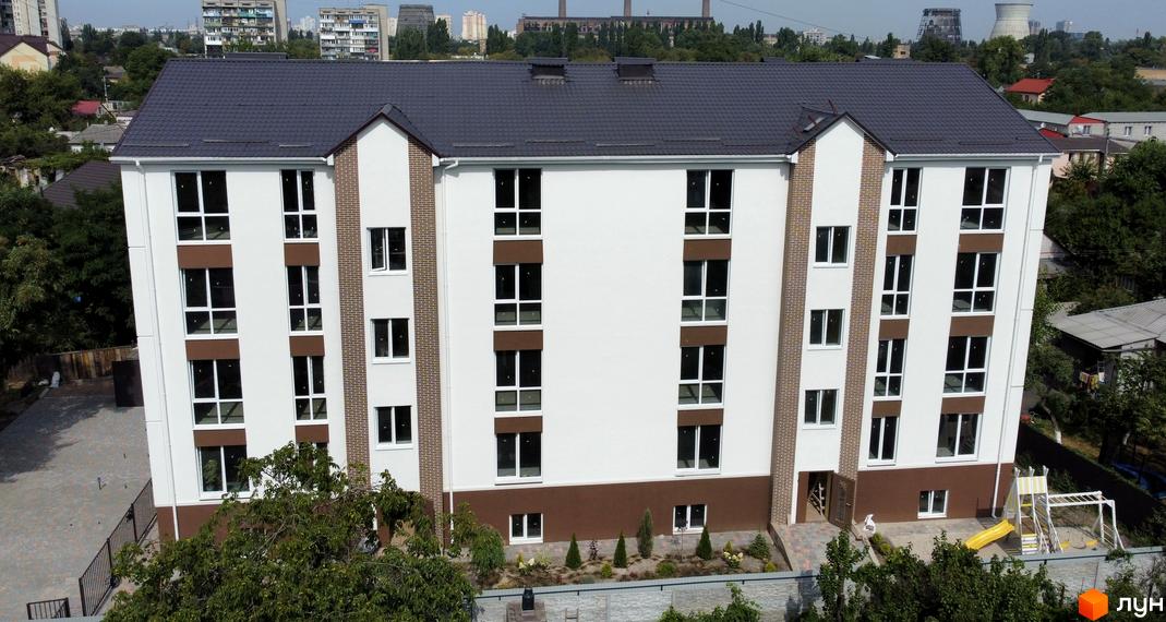 Зовнішній вигляд житлового комплексу ЖК SMART IDEA з біло-коричневим фасадом та великими вікнами, поруч дитячий майданчик та зелені насадження.