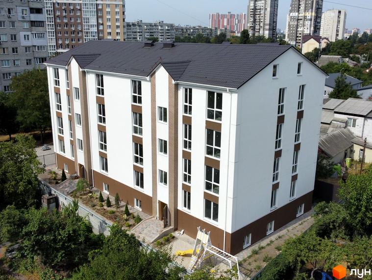 Зовнішній вигляд новобудови ЖК SMART IDEA з білими фасадами та коричневими елементами, прибудинкова територія з зеленими насадженнями та дитячим майданчиком.