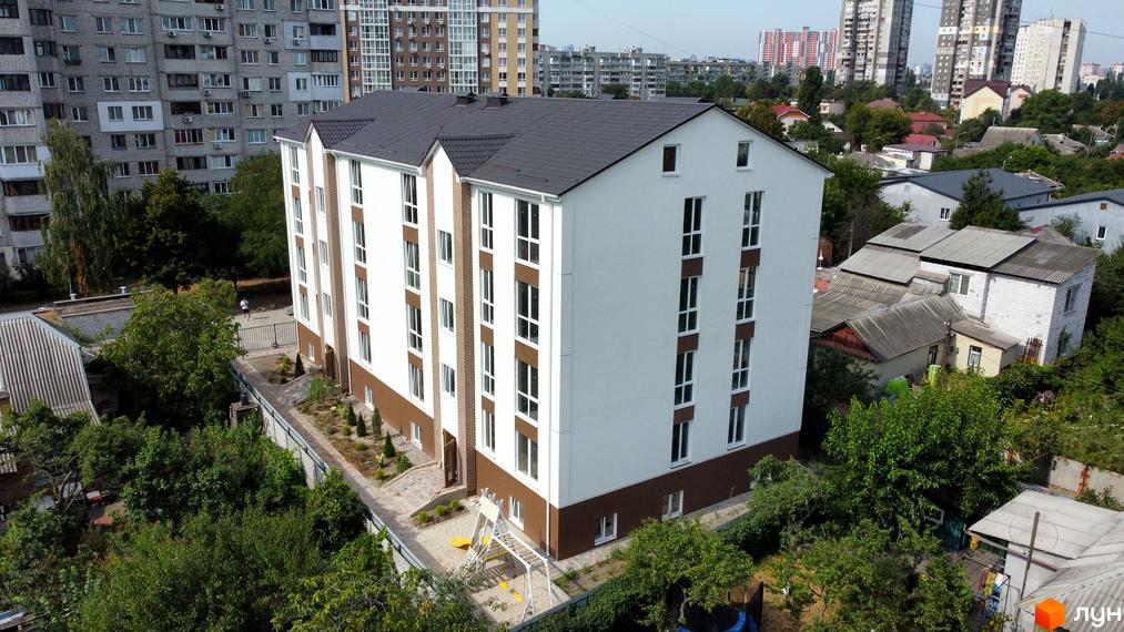 Новобудова ЖК SMART IDEA з біло-коричневим фасадом та темним дахом, поруч дитячий майданчик та зелені насадження.