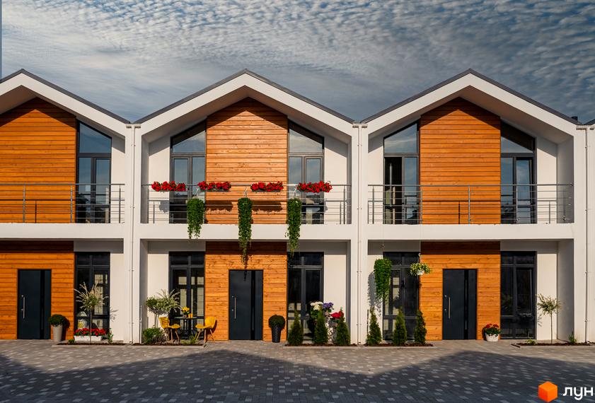 Фасад Котеджного містечка Prydesennya Eco Village з дерев'яним оздобленням та великими вікнами. На території квіти та зелені насадження.