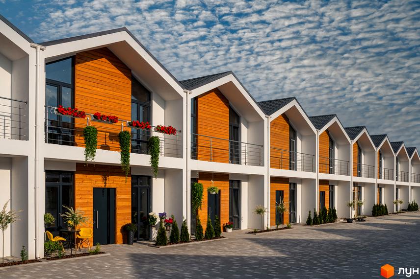 Зображення будинків Котеджного містечка Prydesennya Eco Village з дерев'яним оздобленням та балконами. На подвір'ї бруківка та зелені насадження.