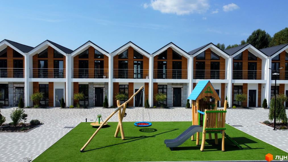 Зображення Котеджного містечка Prydesennya Eco Village: двоповерхові котеджі з дерев'яним оздобленням та дитячий майданчик на зеленій галявині.