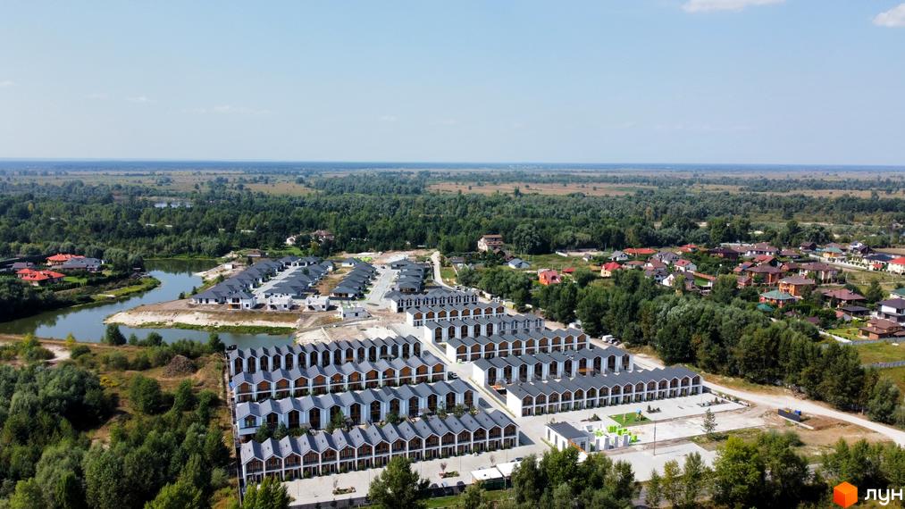 Вигляд з висоти на Котеджне містечко Prydesennya Eco Village з будинками з сірими дахами. Навколо комплексу зелені дерева та озеро.