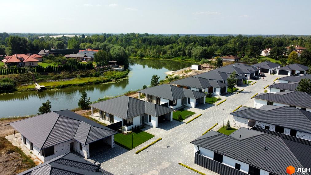 Фото Котеджного містечка Prydesennya Eco Village з висоти пташиного польоту. Будинки з сірими дахами та білими стінами, поруч річка та зелені насадження.