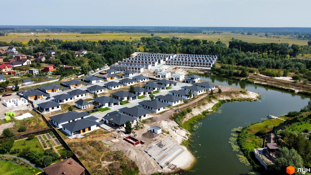 Фото Котеджне містечко Prydesennya Eco Village з будинками з темними дахами та білими стінами, розташованими біля озера.