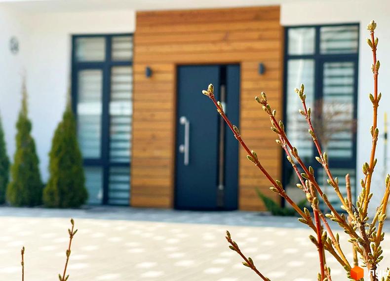 Зовнішній вигляд будинку в Котеджному містечку Prydesennya Eco Village з дерев'яним оздобленням та зеленими насадженнями на подвір'ї.