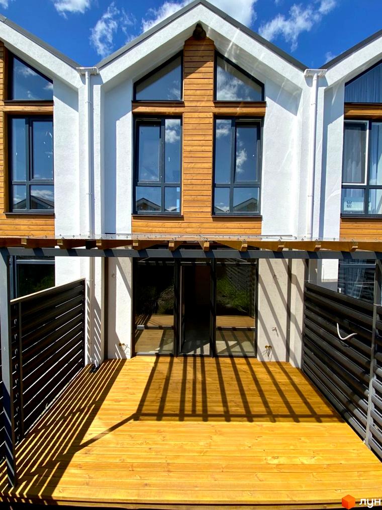 Зовнішній вигляд будинку в Котеджному містечку Prydesennya Eco Village з дерев'яною терасою та чорними огорожами.