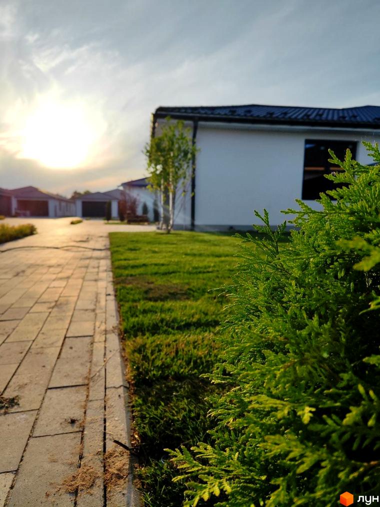 Зображення будинку в Котеджному містечку Prydesennya Eco Village з доглянутим газоном та бруківкою. Вигляд на сонячний краєвид.