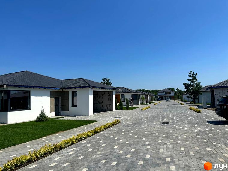 Зображення Котеджного містечка Prydesennya Eco Village: одноповерхові будинки з темними дахами та білими стінами, газон, тротуарна плитка.