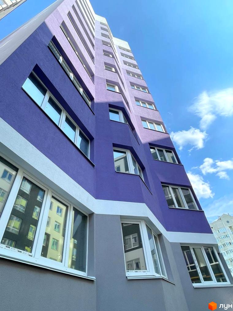 Новобудова Святопетрівський: багатоповерхова будівля фіолетового та сірого кольорів з білими вікнами під блакитним небом.