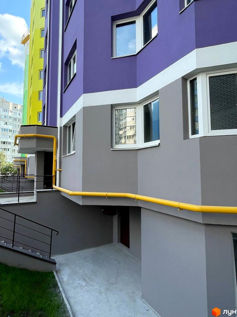 Фасад Житлового комплексу Святопетрівський з фіолетовими, сірими та білими секціями, жовтою газовою трубою. Поруч сходи та зелена трава.