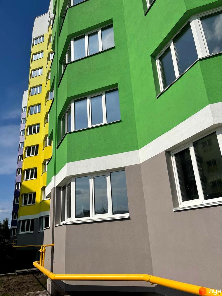 Фасад багатоповерхового будинку Житлового комплексу Святопетрівський з зеленими, жовтими та сірими секціями, білими вікнами. Внизу видно жовті труби.