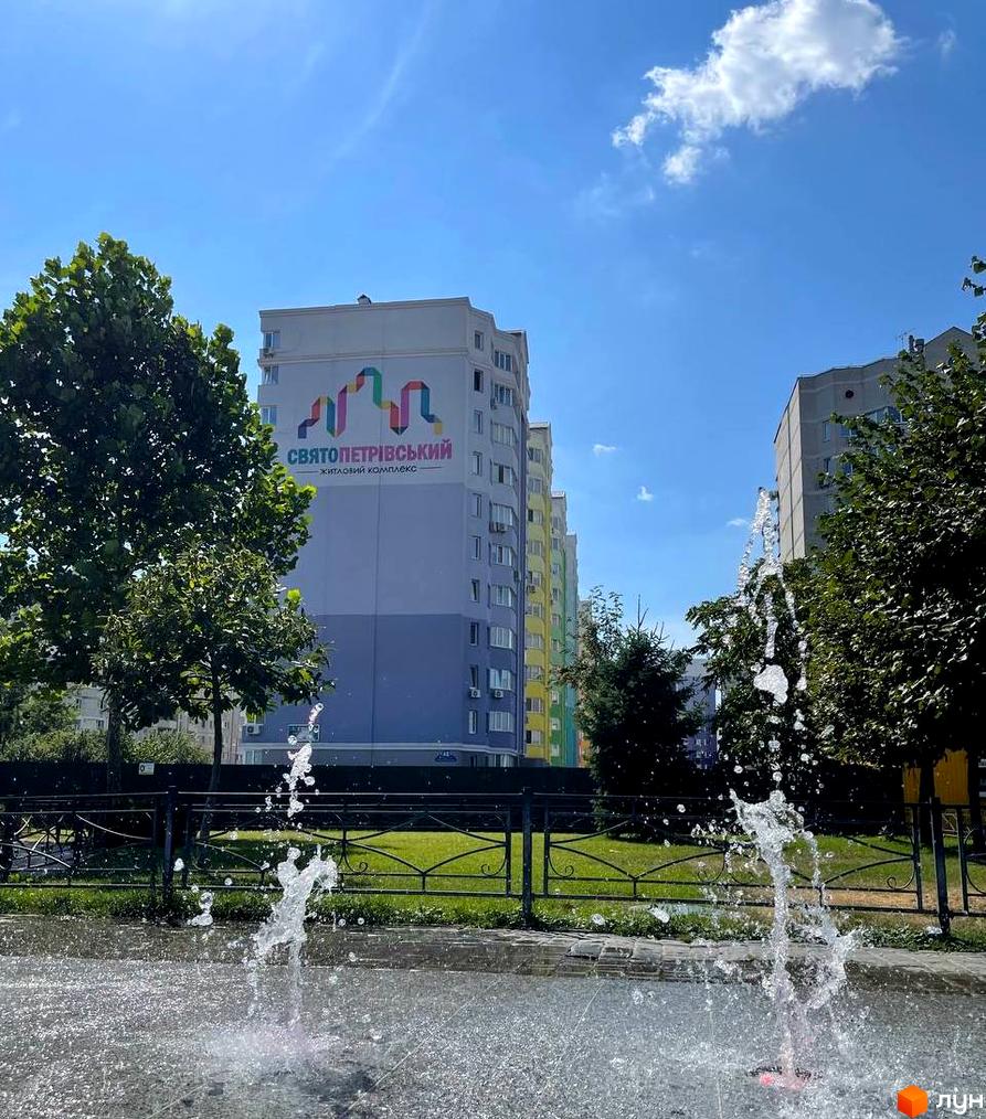 Житловий комплекс Святопетрівський: багатоповерхові будинки з яскравим хвилястим візерунком на фасаді, перед якими розташований фонтан та зелені дерева.