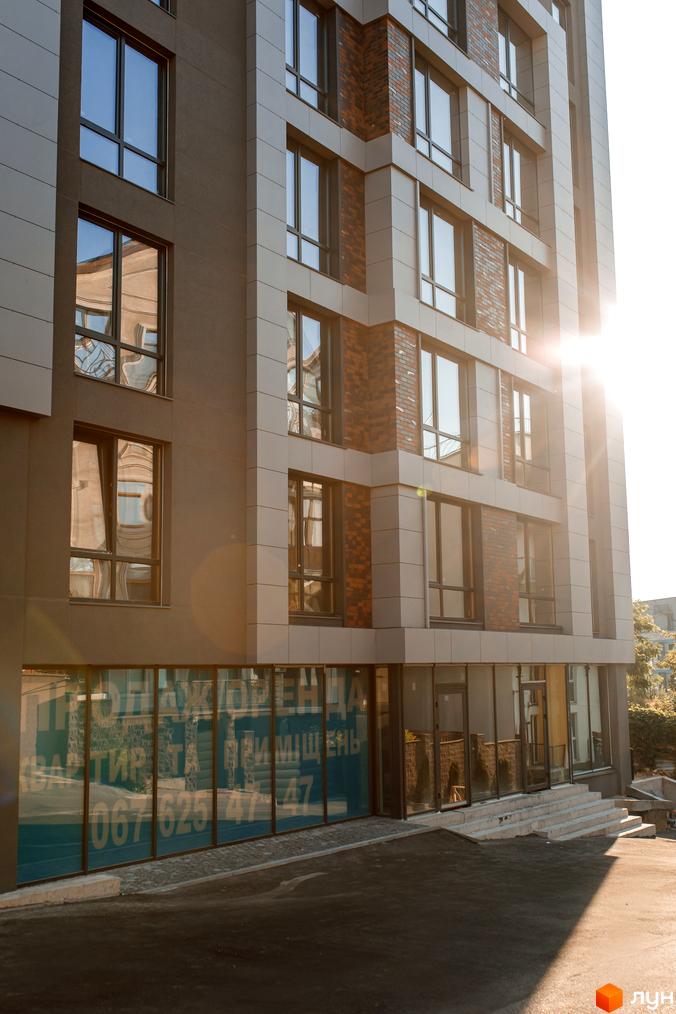 Фасад новобудови ЖК Smart Concept з великими вікнами та цегляними елементами. Біля будинку розташовані сходи та асфальтована територія.