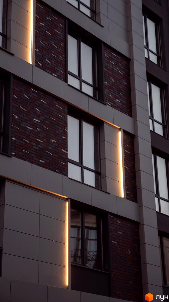 Фасад новобудови ЖК Smart Concept з цегляними та сірими панельними вставками, підсвічений вертикальними лініями теплого світла.