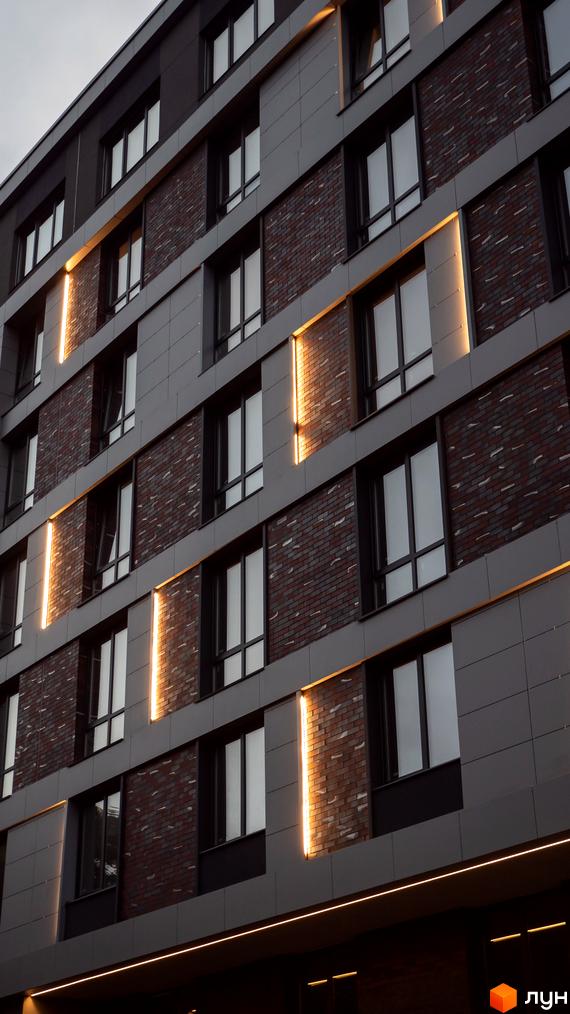 Фасад житлового комплексу Smart Concept з цегляними вставками та вертикальним підсвічуванням. Сучасна архітектура новобудови.