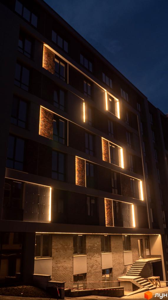 Ефектна підсвітка фасаду житлового комплексу Smart Concept з цегляними вставками. Біля будинку облаштовані сходи та вхідна група.