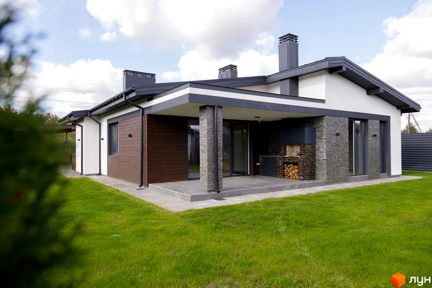 Котеджне містечко КМ New Village. Зовнішній вигляд будинку з коричневою та сірою обробкою, каміном та зеленою прибудинковою територією.