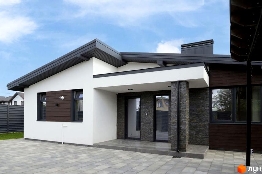 Котеджне містечко КМ New Village: сучасний одноповерховий будинок з темною черепицею та кам'яним оздобленням фасаду, розташований на брукованій прибудинковій території.