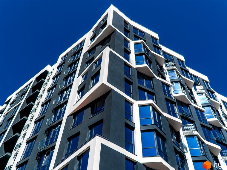 Зображення фасаду багатоповерхового будинку Житловий комплекс Паркова Алея з великими вікнами та балконами на тлі синього неба.