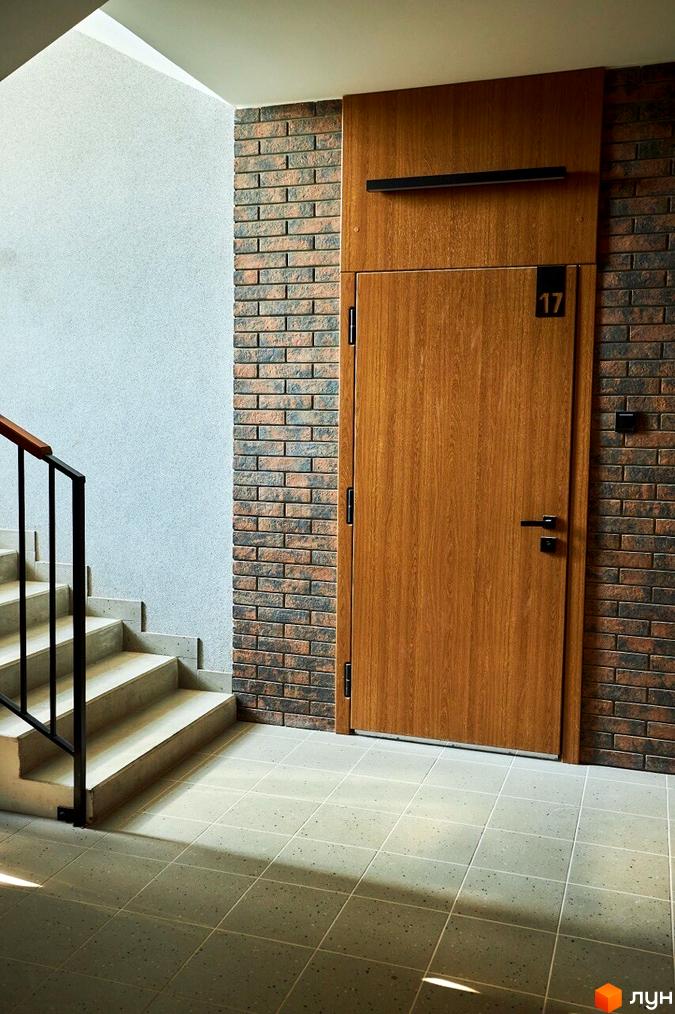 Вхідна група житлового комплексу StyleUP з дерев'яними дверима та цегляною стіною. Сходи ведуть до верхніх поверхів.